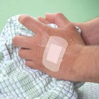 A person's hand with a white, rectangular plaster applied to the skin, demonstrating the product's use.